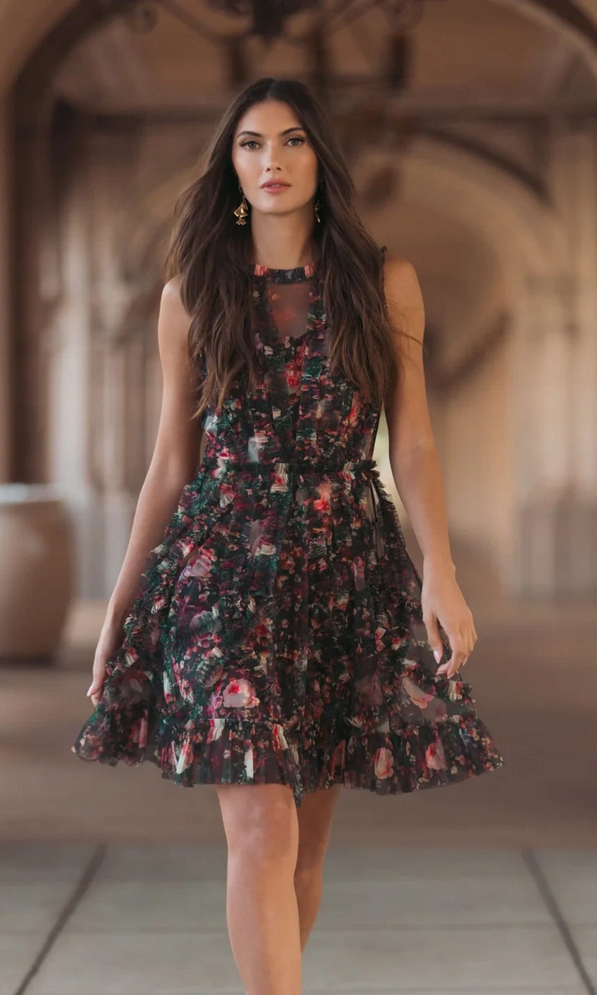 A woman walks confidently indoors against a blurred architectural backdrop, wearing the Mac Duggal 8307 High-Neck Print Wedding-Guest Dress in Black Multi.